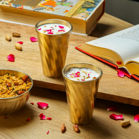Brass Metal Glass Set with lassi and rose petals alongside a book