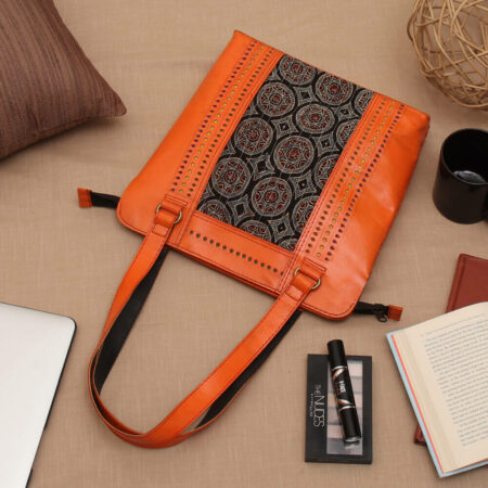 orange handcrafted kutch leather handbag kept on a wooden table. the handbag has ajrakh print