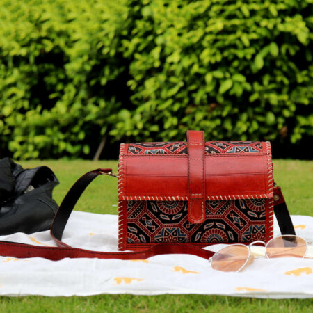 Dome shaped kutch leather Sling Bag brown kept in a garden on a white cloth